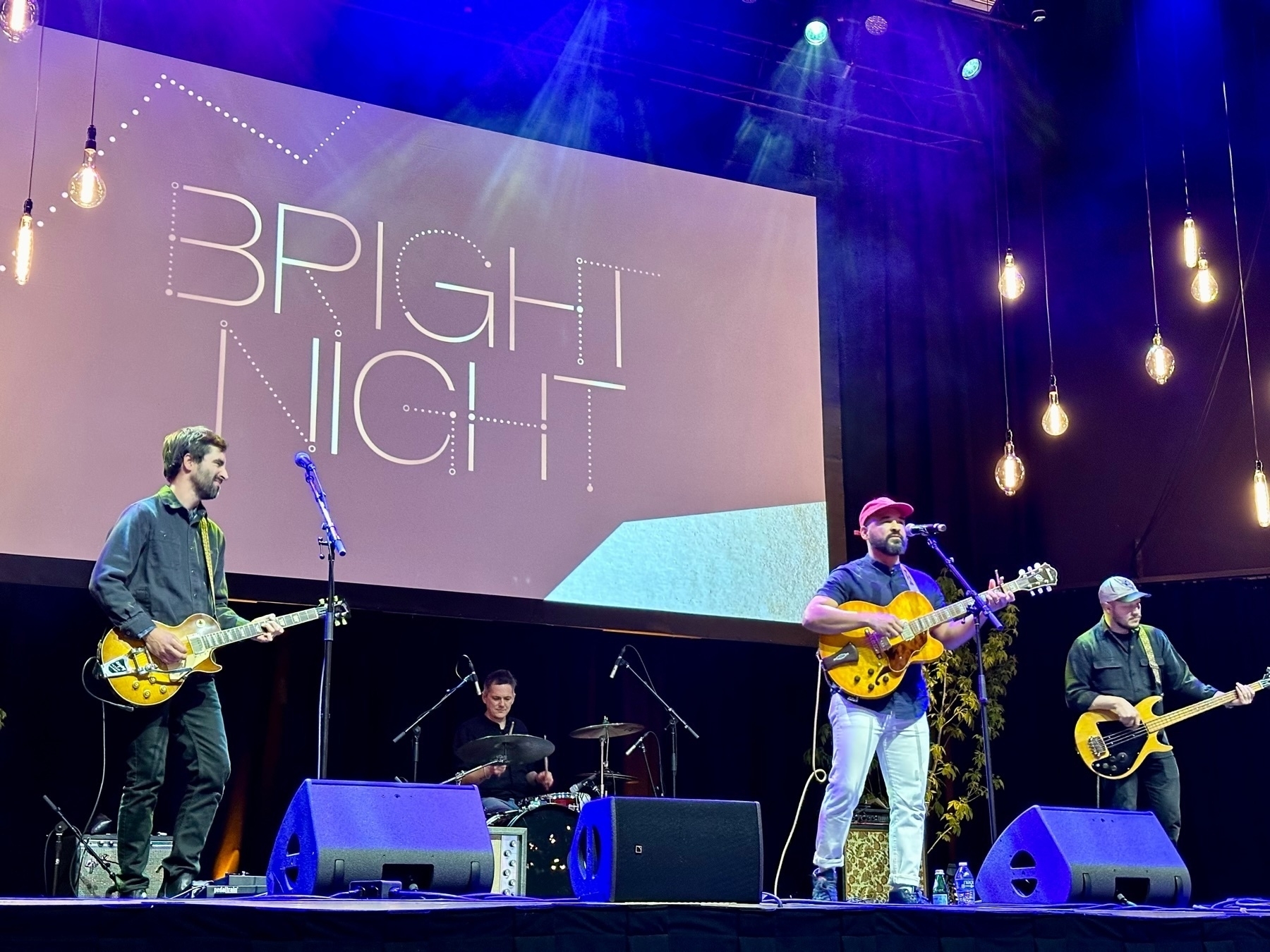 Auto-generated description: A band performs on stage under a sign that reads BRIGHT NIGHT.